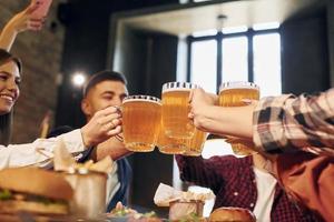 Cheering together. Group of young friends sitting in bar with beer photo