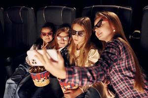 Holding phone in hand. Group of kids sitting in cinema and watching movie together photo