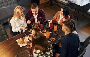 tener una conversación grupo de jóvenes amigos sentados juntos en el bar con cerveza foto