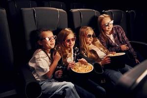 Weekend fun. Group of kids sitting in cinema and watching movie together photo