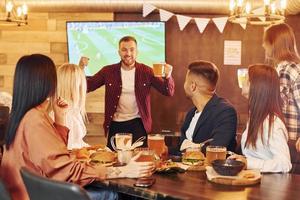 sosteniendo vasos. grupo de jóvenes amigos sentados juntos en el bar con cerveza foto