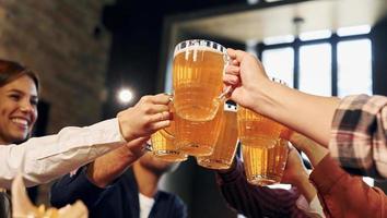 Cheering together. Group of young friends sitting in bar with beer photo