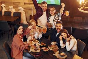 adentro en el bar. grupo de jóvenes amigos sentados juntos con cerveza foto