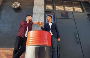 dos amigos parados afuera y sosteniendo vasos con cerveza foto