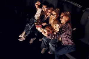 sosteniendo el teléfono en la mano. grupo de niños sentados en el cine y viendo películas juntos foto