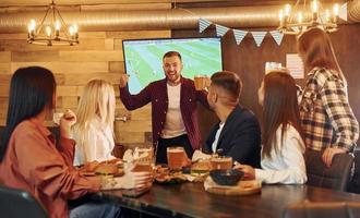 contra la televisión grupo de jóvenes amigos sentados juntos en el bar con cerveza foto