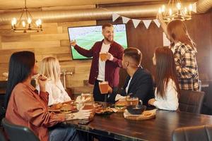 Against TV. Group of young friends sitting together in bar with beer photo