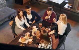 comiendo y bebiendo. grupo de jóvenes amigos sentados juntos en el bar con cerveza foto