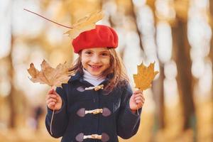 In a red beret. Cute positive little girl have fun in the autumn park photo