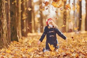 Throwing leaves into the air. Cute positive little girl have fun in the autumn park photo