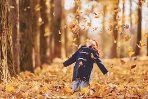 lanzando hojas al aire. linda niña positiva diviértete en el parque de otoño foto