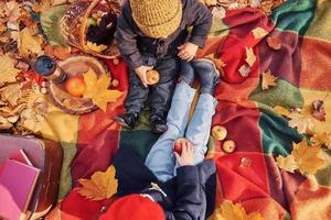 Little boy with his sister is sitting on the ground in the autumn park photo