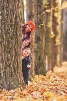 escondiéndose detrás de un árbol. madre con su hijo pequeño y su hija se divierten en el parque de otoño foto