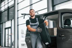 con neumático en las manos. el hombre uniformado está trabajando en el autosalón durante el día foto