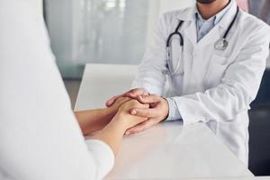 Holding customer by the hands. Professional medic in white coat is in the clinic photo