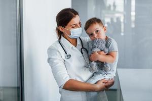 con un niño pequeño en las manos. médico profesional en bata blanca está en la clínica foto