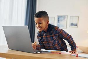 With laptop. Cheerful young boy is at home alone photo