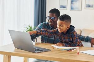 usando una computadora portátil padre afroamericano con su hijo pequeño en casa foto