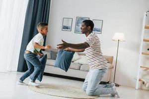 pelea de almohadas. padre afroamericano con su hijo pequeño en casa foto