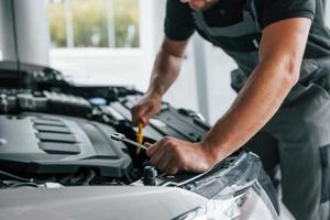 Some problems under the hood. Man in uniform is working in the autosalon at daytime photo