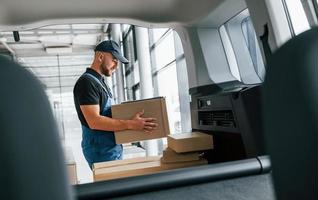 With vehicle. Delivery man in uniform is indoors with car and with order photo