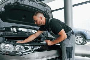 Under the hood. Man in uniform is working in the autosalon at daytime photo