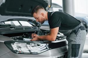 Repairing of the car. Man in uniform is working in the autosalon at daytime photo