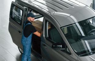 Walking and holding box in hands. Delivery man in uniform is indoors with car and with order photo