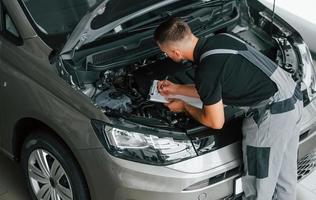 Engine repair. Man in uniform is working in the autosalon at daytime photo