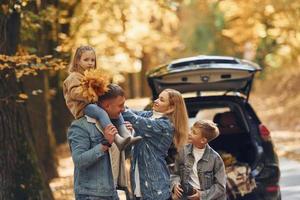 Near car with open trunk. Happy family is in the park at autumn time together photo