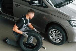 Installing new tire. Man in uniform is working in the autosalon at daytime photo