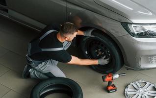 instalando un neumático nuevo. el hombre uniformado está trabajando en el autosalon durante el día foto