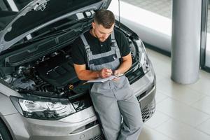 Engine repair. Man in uniform is working in the autosalon at daytime photo