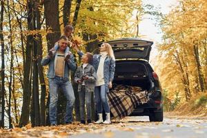 el coche está detrás. la familia feliz está en el parque en otoño juntos foto