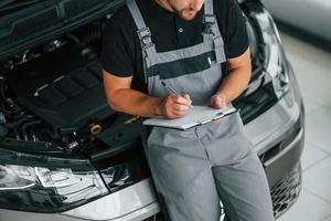 cerca del coche. el hombre de uniforme está trabajando en el autosalón durante el día foto