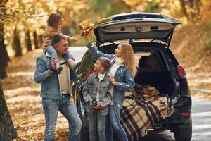 Near car with open trunk. Happy family is in the park at autumn time together photo