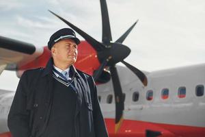 Pilot in formal black uniform is standing outdoors near plane photo