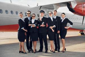 posando para una cámara. tripulación de trabajadores del aeropuerto y del avión con ropa formal de pie juntos al aire libre foto