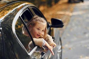 Little girl sitting in the black automobile and looking through the window photo