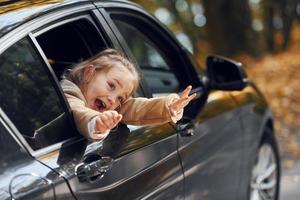 Little girl sitting in the black automobile and looking through the window photo