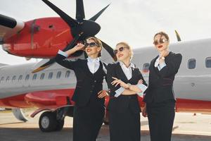 Three stewardesses. Crew of airport and plane workers in formal clothes standing outdoors together photo