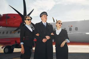 tres personas. tripulación de trabajadores del aeropuerto y del avión con ropa formal de pie juntos al aire libre foto