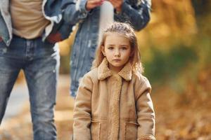 Little girl with her parents. Happy family is in the park at autumn time together photo