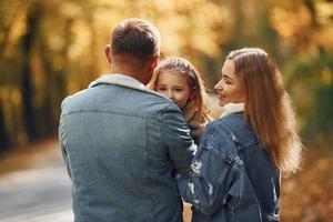 Little girl with her parents. Happy family is in the park at autumn time together photo