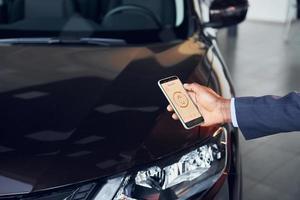 usando el teléfono inteligente para abrir la puerta. joven empresario afroamericano en traje negro es el autosalon foto