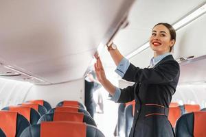 Young stewardess that is in formal black clothes is standing indoors in the plane photo