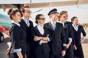 cerca del avión. tripulación de trabajadores del aeropuerto con ropa formal de pie juntos al aire libre foto