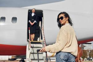 Young female passanger in casual clothes is outdoors near the plane photo