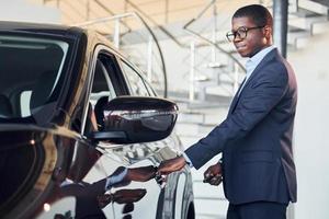 abriendo la puerta. joven empresario afroamericano en traje negro es el autosalon foto