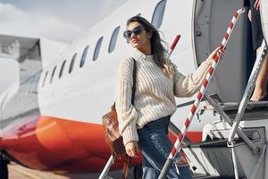 With lugagge. Young female passanger in casual clothes is outdoors near the plane photo